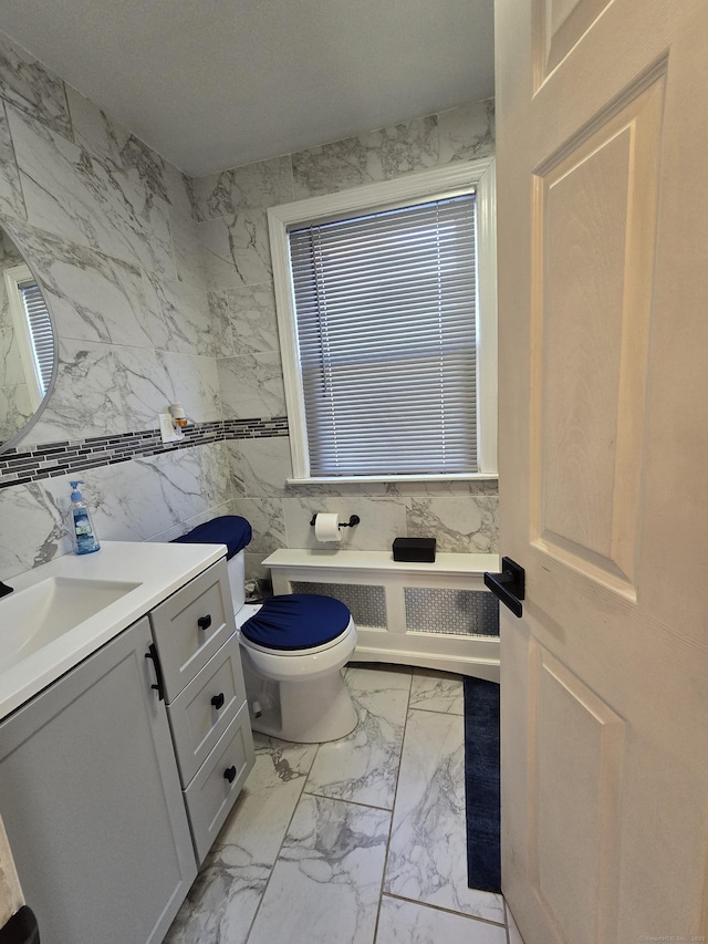 half bathroom featuring radiator, marble finish floor, toilet, and vanity