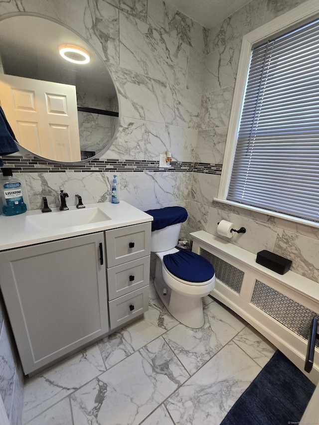 bathroom with toilet, radiator heating unit, marble finish floor, vanity, and tile walls