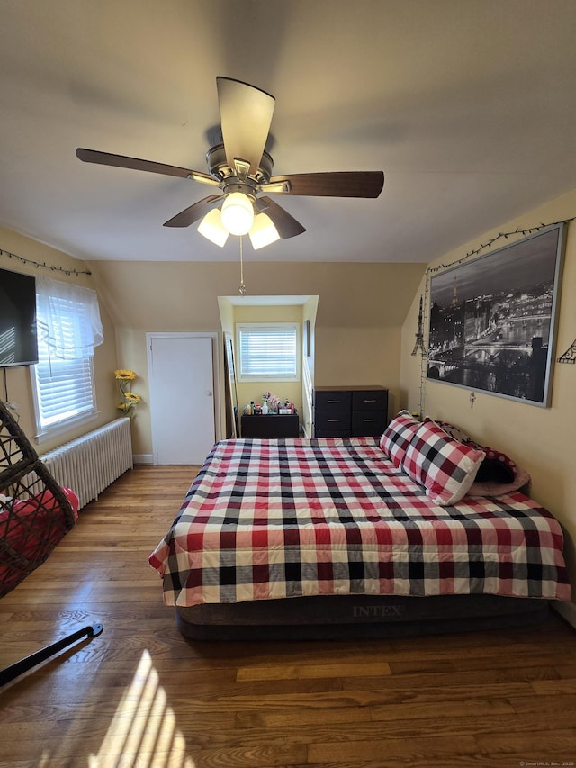 bedroom with radiator, ceiling fan, multiple windows, and wood finished floors