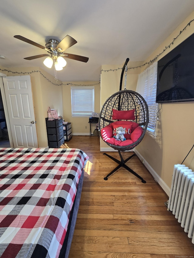 bedroom with radiator, ceiling fan, baseboards, and wood finished floors