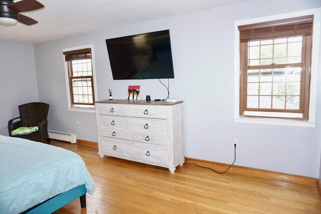 bedroom with a baseboard heating unit, light wood-style flooring, and baseboards