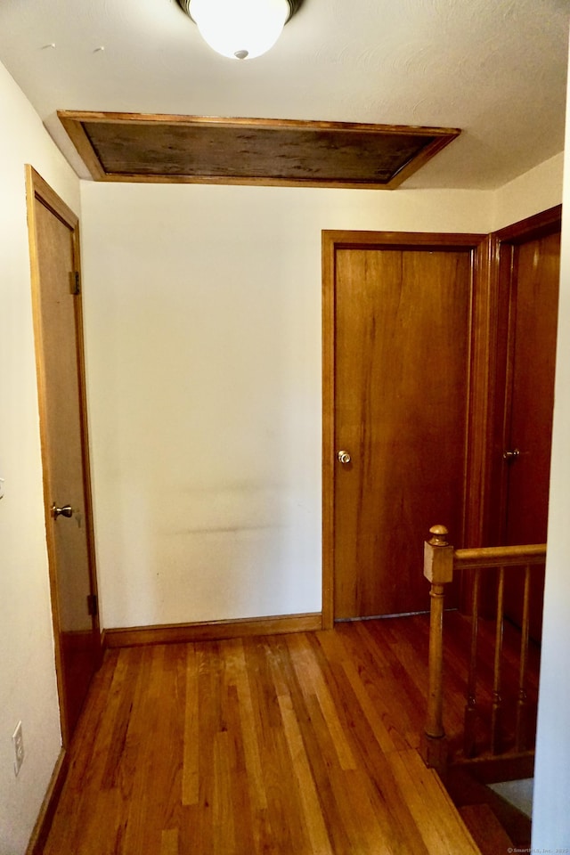 corridor with wood finished floors, an upstairs landing, and baseboards