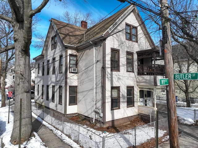 snow covered property with a chimney, cooling unit, fence, and a balcony