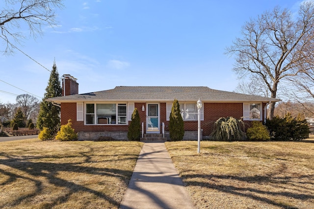 view of front facade with a shingled roof, a front lawn, brick siding, and a chimney