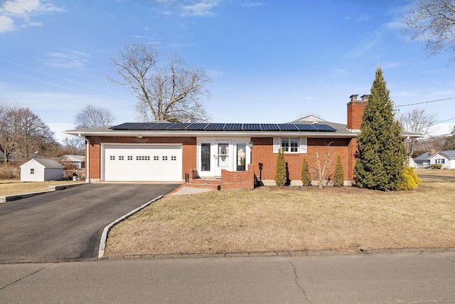 ranch-style home with solar panels, a chimney, a garage, aphalt driveway, and brick siding