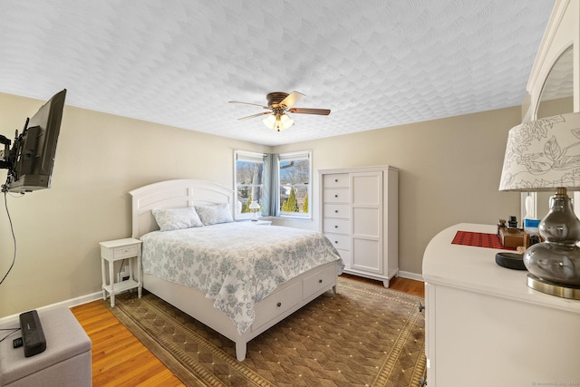 bedroom with a textured ceiling, a ceiling fan, baseboards, and wood finished floors