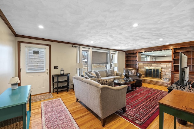 living area with light wood-type flooring, a textured ceiling, a stone fireplace, and crown molding