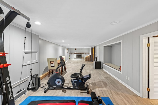 workout area featuring a fireplace with raised hearth, crown molding, baseboards, and wood finished floors