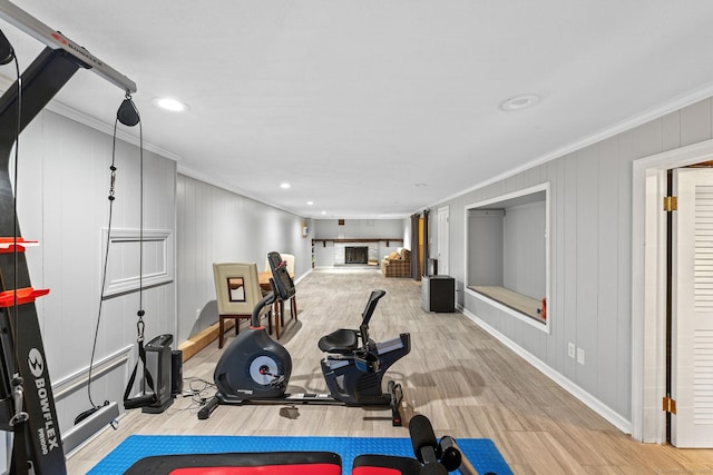 exercise room with crown molding, a fireplace with raised hearth, baseboards, and wood finished floors