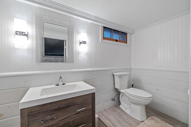 half bath featuring toilet, ornamental molding, wood finished floors, and vanity