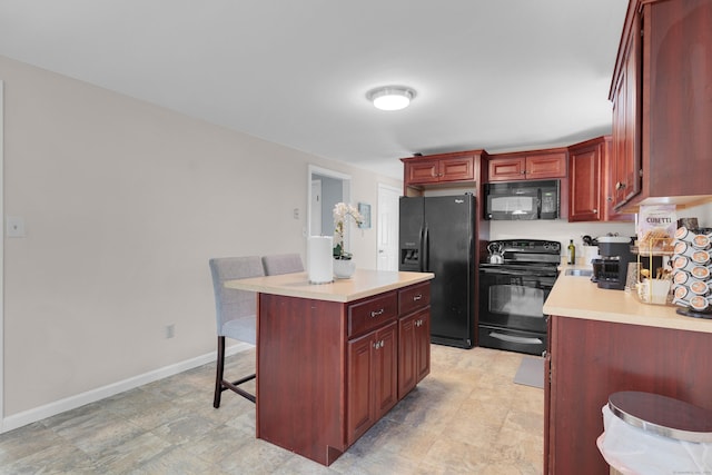 kitchen with a breakfast bar, baseboards, light countertops, reddish brown cabinets, and black appliances