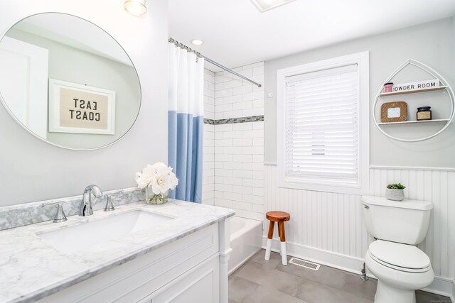 full bath featuring toilet, shower / bathtub combination with curtain, vanity, and wainscoting