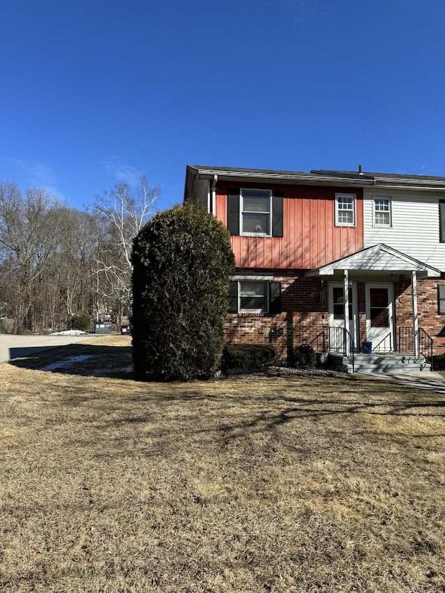 exterior space featuring brick siding, board and batten siding, and a front yard