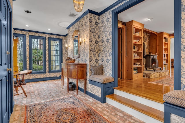 entryway featuring brick floor, visible vents, crown molding, and wallpapered walls