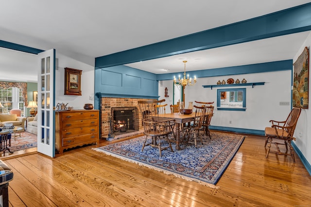 dining area featuring baseboards, hardwood / wood-style floors, beam ceiling, a fireplace, and an inviting chandelier