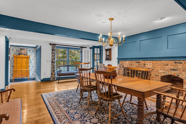 dining room featuring light wood-type flooring, a decorative wall, baseboards, a brick fireplace, and a chandelier