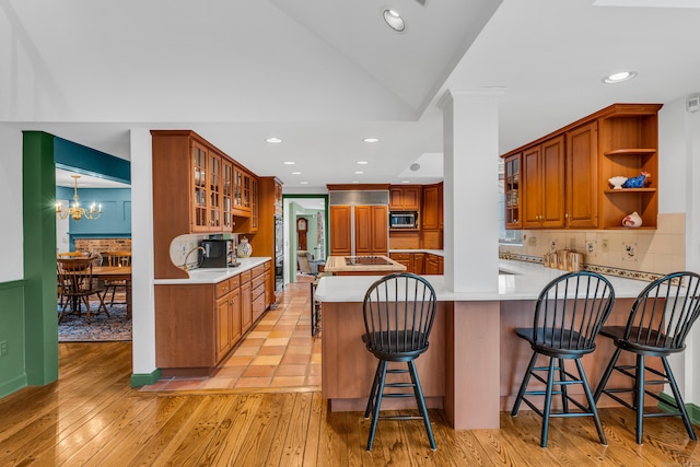 kitchen with light wood finished floors, a peninsula, open shelves, glass insert cabinets, and stainless steel microwave