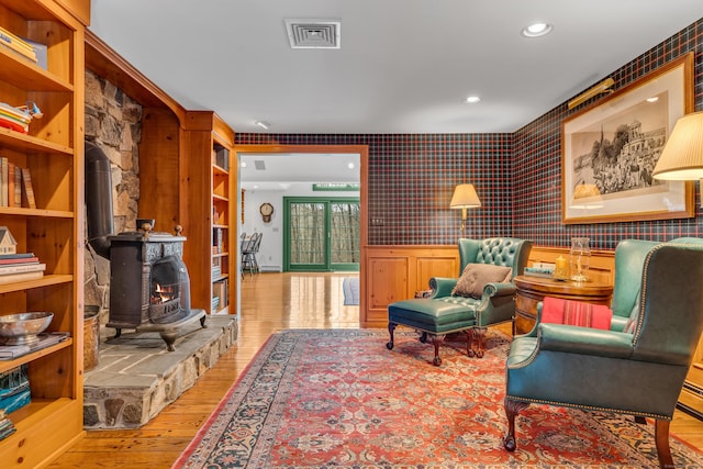 sitting room with visible vents, wallpapered walls, wainscoting, a wood stove, and wood finished floors