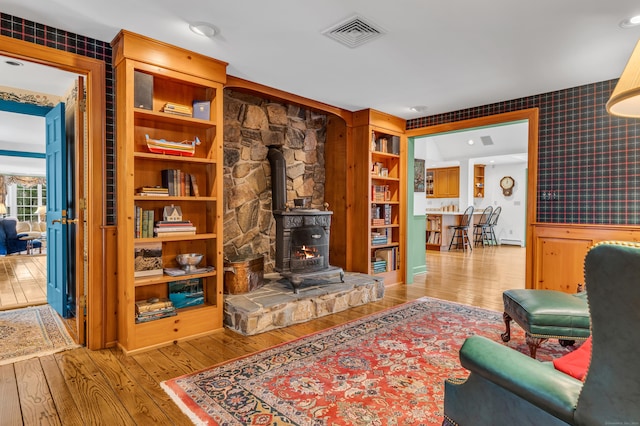 living area featuring visible vents, wallpapered walls, wainscoting, a wood stove, and hardwood / wood-style flooring