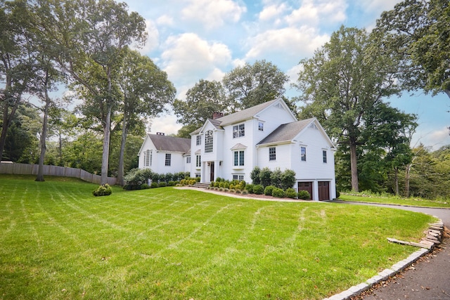 colonial house with a garage, driveway, a chimney, fence, and a front lawn