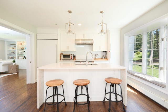 kitchen with dark wood-style floors, decorative light fixtures, under cabinet range hood, and a kitchen breakfast bar