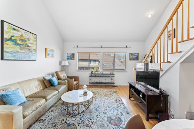 living area with light wood-type flooring, vaulted ceiling, baseboards, and stairs