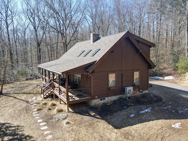 view of side of home featuring a view of trees, roof with shingles, and a chimney