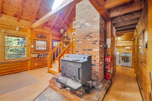 unfurnished living room featuring washing machine and dryer, lofted ceiling with beams, a wood stove, and wood finished floors