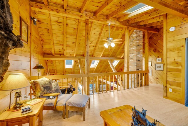 living area featuring wood finished floors, vaulted ceiling with skylight, wooden ceiling, wood walls, and ceiling fan