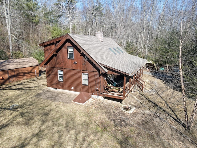 back of house with a shingled roof, an outdoor structure, and a chimney