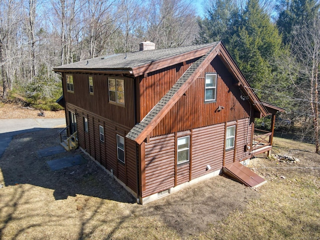 view of side of home featuring roof with shingles, a chimney, and faux log siding