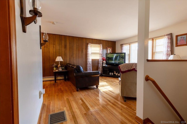 living room featuring light wood-style flooring, a baseboard radiator, visible vents, and wooden walls