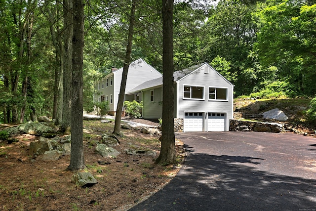 view of property exterior featuring an attached garage, aphalt driveway, and a view of trees