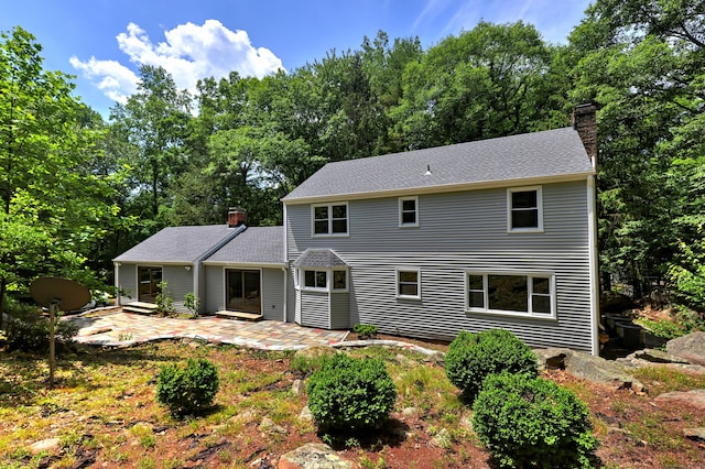 back of house with a shingled roof, a patio area, and a chimney