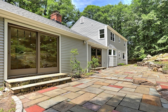 rear view of property with entry steps, a patio area, a chimney, and roof with shingles