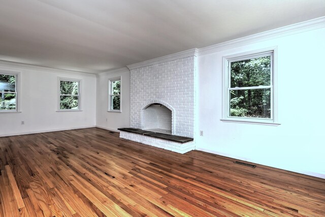 unfurnished living room featuring visible vents, ornamental molding, a brick fireplace, wood finished floors, and baseboards