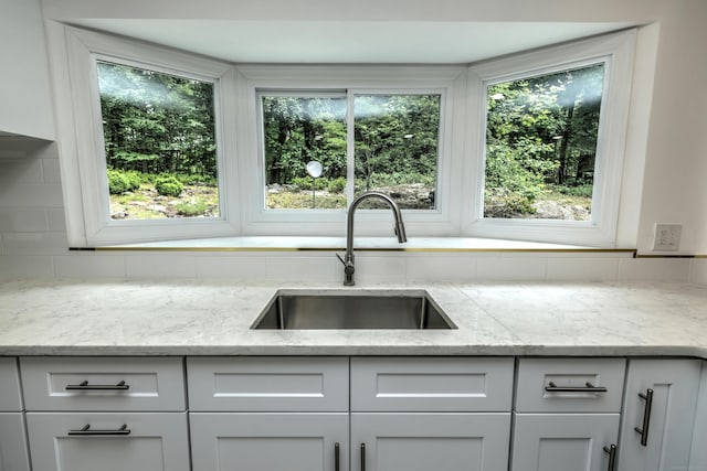 kitchen with white cabinetry, a healthy amount of sunlight, a sink, and light stone countertops