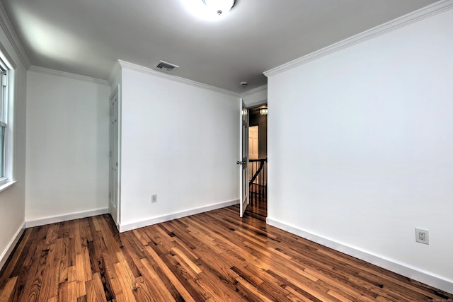 spare room with dark wood-style floors, visible vents, ornamental molding, and baseboards