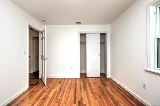 unfurnished bedroom with a closet, visible vents, baseboards, and wood finished floors