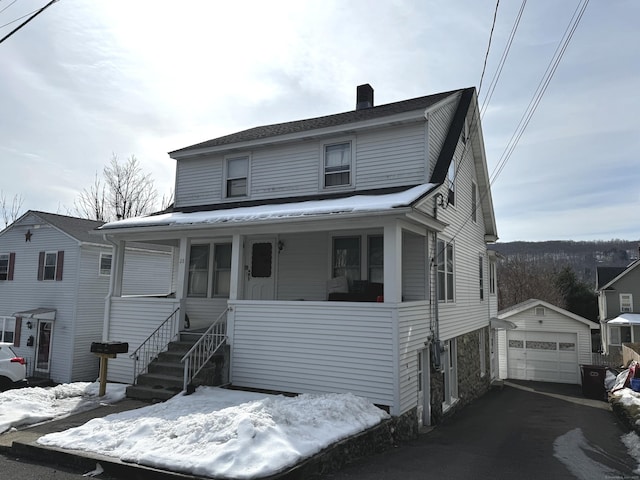 view of front of house featuring a garage, a chimney, aphalt driveway, an outbuilding, and a porch