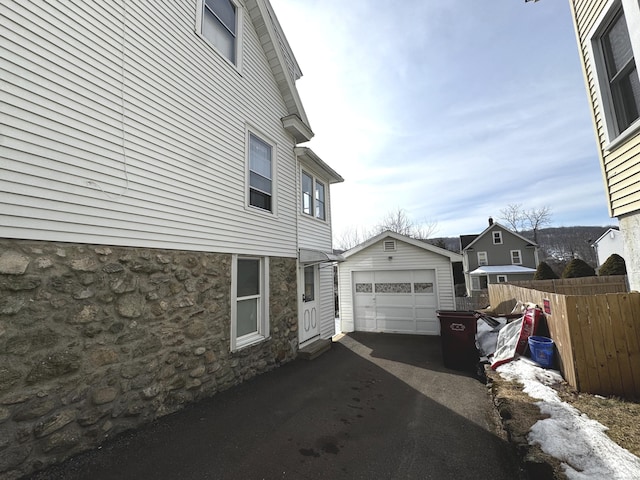 view of side of property with aphalt driveway, an outdoor structure, fence, and a detached garage