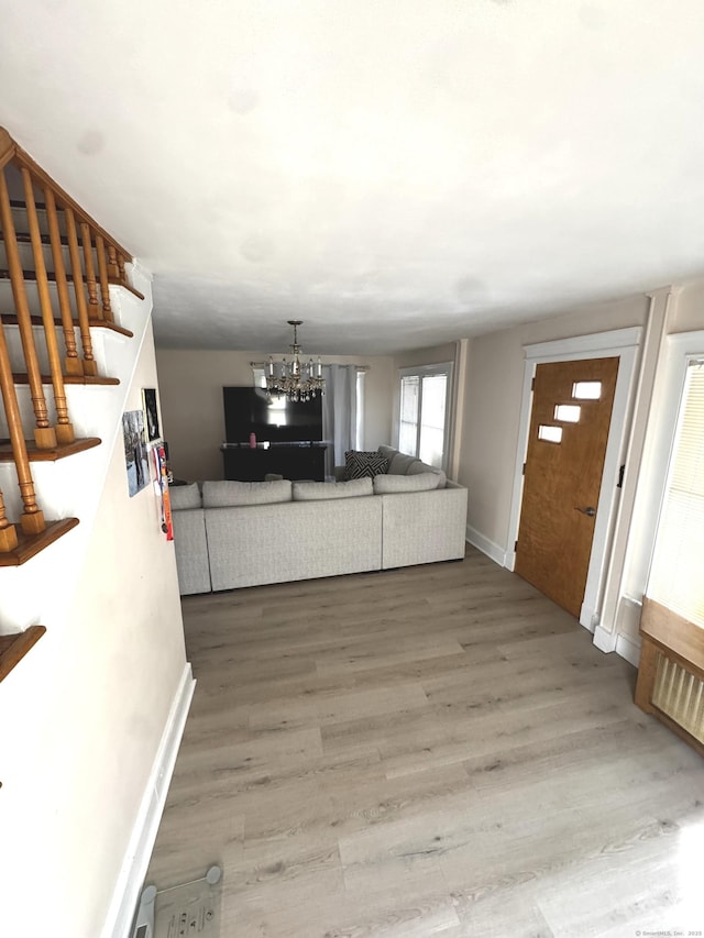 unfurnished living room with stairs, a chandelier, baseboards, and wood finished floors