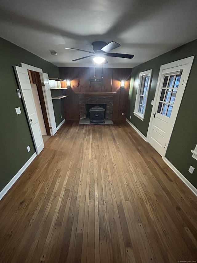 unfurnished living room with a wood stove, ceiling fan, baseboards, and dark wood finished floors