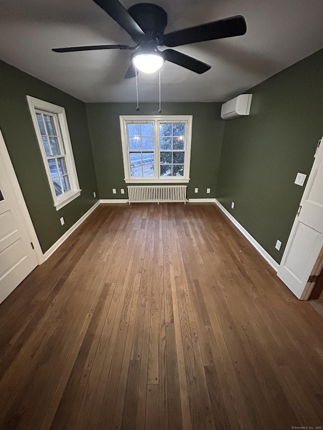 interior space with a wall unit AC, a ceiling fan, baseboards, dark wood-style floors, and radiator heating unit