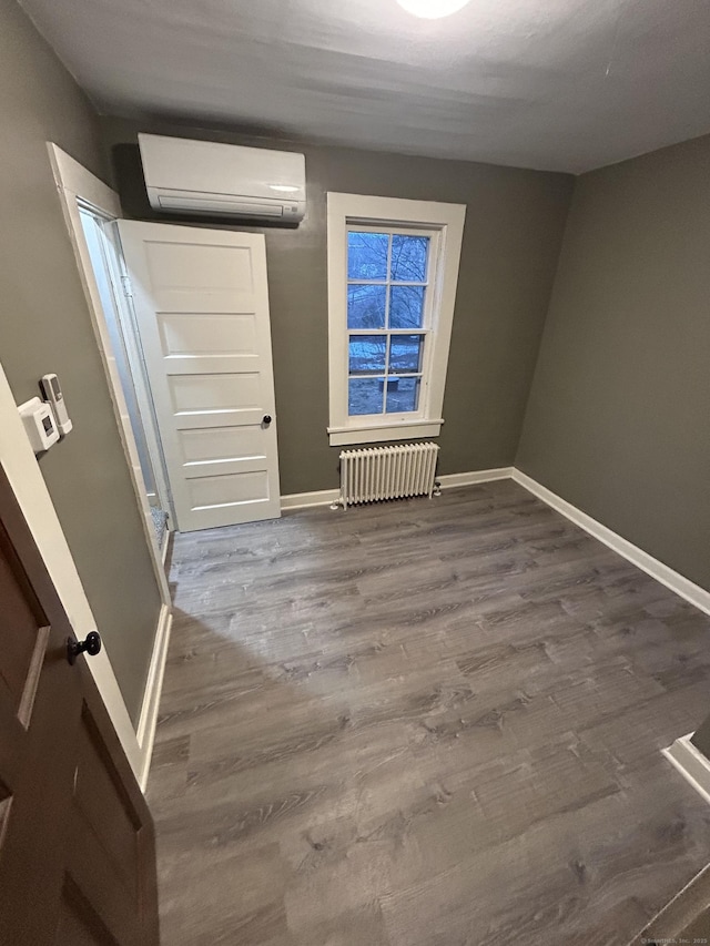 interior space featuring radiator, a wall unit AC, baseboards, and wood finished floors