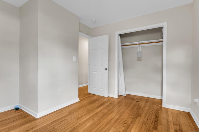 unfurnished bedroom featuring light wood finished floors, baseboards, and a closet