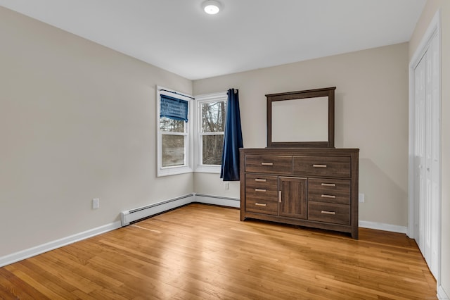 unfurnished bedroom with baseboard heating, light wood-type flooring, a closet, and baseboards