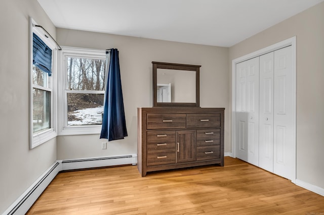 unfurnished bedroom featuring light wood-type flooring, a baseboard radiator, and a closet