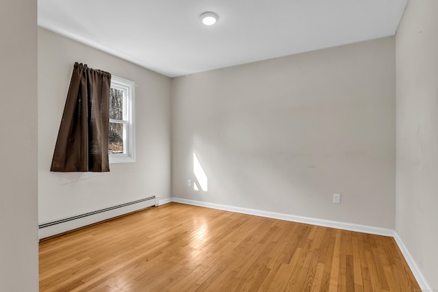 empty room featuring light wood finished floors, a baseboard radiator, and baseboards