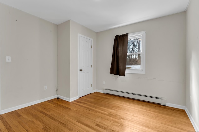 spare room featuring light wood-style floors, a baseboard radiator, and baseboards